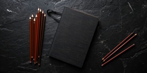Set of brown pencils and notebook placed on black stone surface for artistic activities