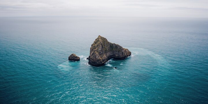 Large rock formation in blue waters, erosion risk on coastal landscapes during summer travel