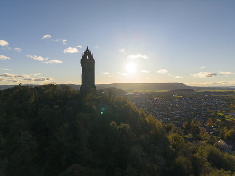 Aerial view of the silhouette of the Wallace Monument atop Abbey Craig hill against a backdrop of Stirling city under a bright sky., Stirling, Scotland, United Kingdom.