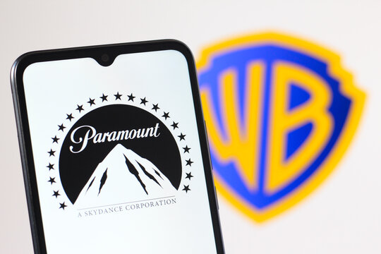 In this photo illustration, the Paramount logo is seen displayed on a smartphone screen and the Warner Bros Discovery logo in the background.