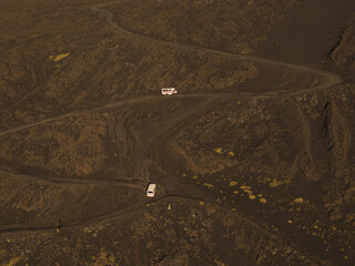 Aerial view of vehicles navigating the dark, volcanic landscape, a stark contrast to the sparse vegetation clinging to the slopes, Mount Etna, Sicilia, Italy.