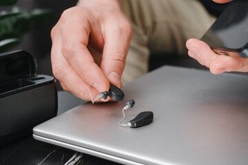 Modern digital hearing aids, smartphone and charging case on a sleek office table, with person preparing devices for work. Business setting, accessibility and professional lifestyle. Man use earbuds 