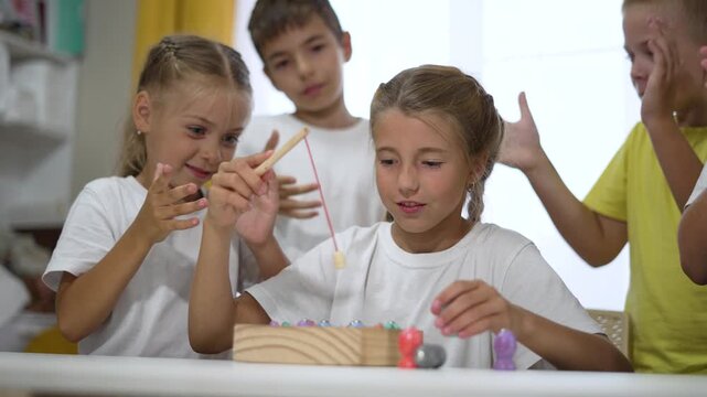 Children play wooden fishing game at classroom table while kid and child friend cheer and clap as player uses toy rod to catch colorful fish during birthday party for teamwork play and social learning