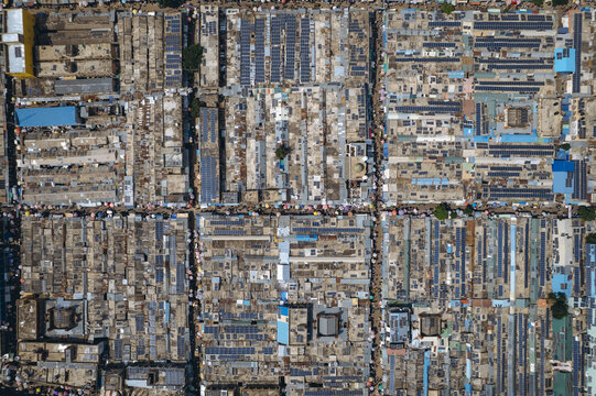 Aerial view of a dense urban sprawl, rooftops a mosaic of textures under the sun, vibrant blue pools punctuate the scene, Kano, Kano, Nigeria.