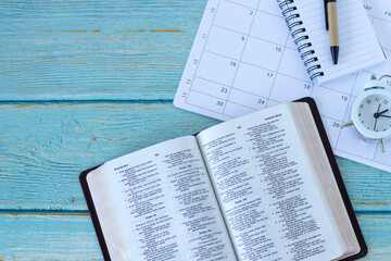 Open holy bible book with calendar, alarm clock and notebook. Top view. Copy space. Christian Scripture study, time, and patience, biblical concept.