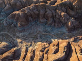 Aerial view of sculpted earth tones painted by shadows and light, creating a tapestry of textures and hues across the arid landscape, Nazlini, Arizona, United States.