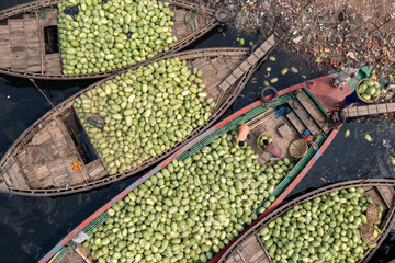 Aerial view of boats brimming with pale green produce drift on dark waters amidst scattered debris, Dhaka, Dhaka Division, Bangladesh.