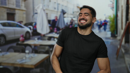 Young man smiling outdoors on a restaurant terrace, showcasing casual style and vibrant energy in...