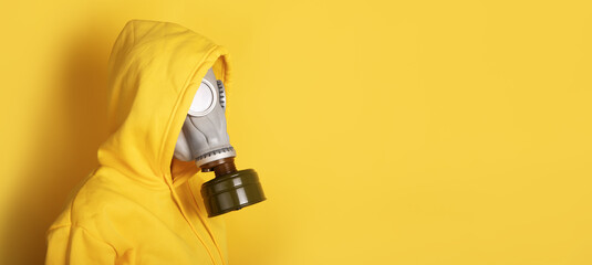 Side view of person wearing grey gas mask and yellow hoodie against matching yellow background, copy space.