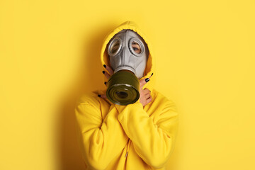 Individual wearing a gray gas mask and yellow hoodie, posing against a vibrant yellow background. Modern, bold, and eye-catching composition.