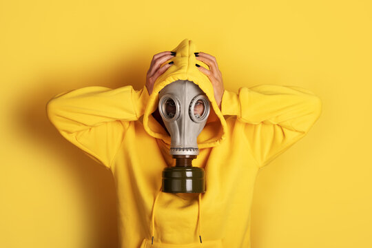 Individual wearing a gray gas mask and yellow hoodie against a yellow background, creating a bold and modern visual statement. - Powered by Adobe
