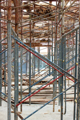 Hallway path between rows of steel scaffolding and stacks of wooden planks on the ground floor of a building construction site.