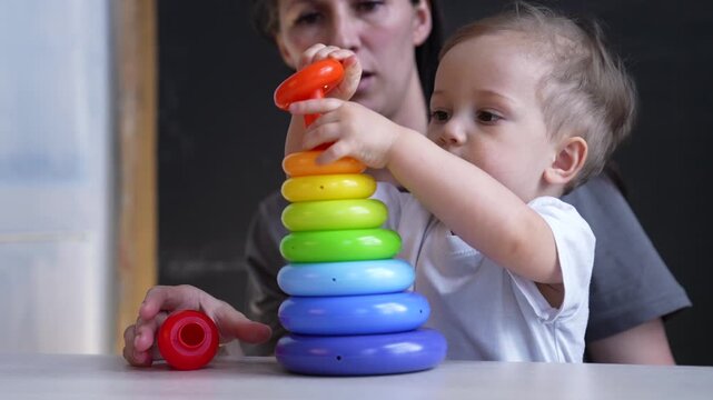 Toddler stacking colorful ring toy while mother guides hand and caregiver watches attentively child concentrates on play and learning with rainbow ring set bright skill development and parent child