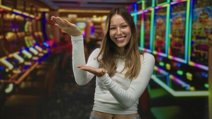 Woman smiling with palms up presenting near slot machines in a colorful casino interior; joy...