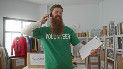 Man in green volunteer shirt smiling and holding clipboard and phone to ear in modern building donation center; charity dedication.