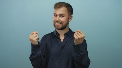 Man smiling showing hands with pinched fingers gesture against light blue studio wall; playful invitation.