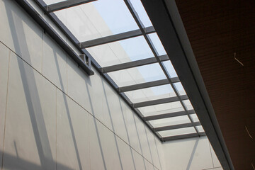 Obraz premium Modern glass roof skylight supported by dark horizontal steel beams, installed over light gray panel walls, allowing natural light into the interior.