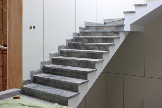 Modern interior staircase with veined gray marble treads and an open stringer, set between clean white walls in a bright indoor space.