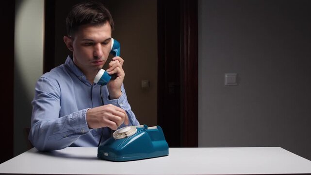Man presses rotary phone, Focused individual engages vintage telephone, Man carefully operates retro teal rotary dialing device, Person diligently uses oldfashioned rotary phone in studio environment