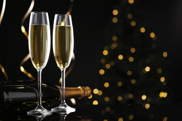 Merry Christmas and Happy New Year. Flute glasses with sparkling wine, serpentine streamers and bottle on black background against blurred lights. Space for text