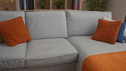 Soft grey sofa with orange cushion and matching textured throw in spacious building flanked by wooden bookshelf; serenity.
