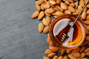Delicious honey in glass bowl, dipper and almonds on dark textured table, flat lay. Space for text
