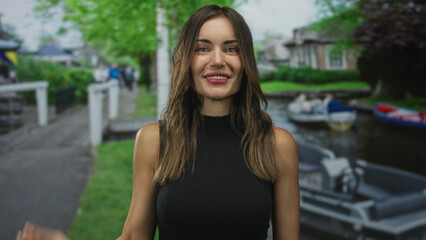 Fototapeta premium Young hispanic woman shades eyes with hand on amsterdam canal street while looking toward the sunlight; curiosity.
