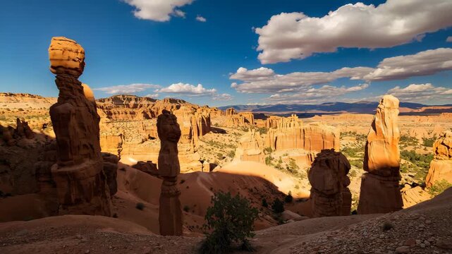 Wide view of unique rock formations in red sandstone landscape under bright blue sky with fluffy clouds showcasing tall hoodoos casting shadows against the warm desert tones in daylight