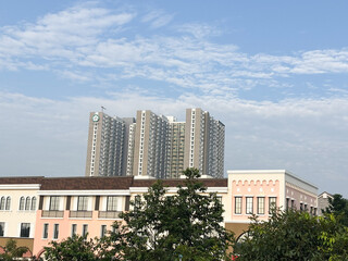A modern high-rise apartment or condominium complex featuring multiple towers, standing tall against a bright blue sky with scattered wispy clouds.