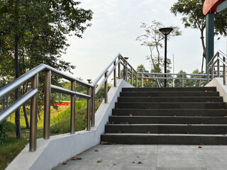 A low-angle, outdoor shot capturing a concrete staircase with modern, polished stainless steel railings ascending toward the top.