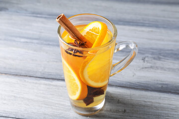 Delicious mulled white wine with slices of orange and spices in glass cup on grey wooden table, closeup