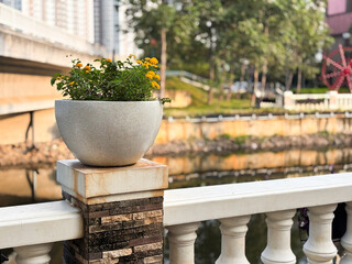 A close-up, horizontal shot focusing on a decorative stone planter with bright yellow-orange flowers (likely Lantana) resting on a patterned pillar.