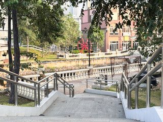 A wide-angle, low-perspective shot looking down a flight of outdoor stone stairs with stainless steel railings leading into a partially shaded park area.