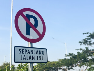 A close-up shot of an Indonesian traffic sign indicating "No Parking" (P with a red circle and diagonal line) with a supplementary plate below it that reads "SEPANJANG JALAN INI"