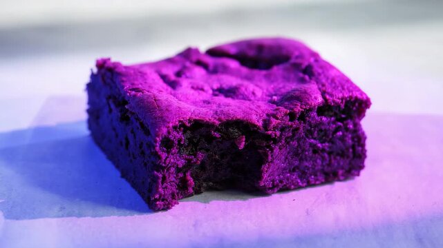 Close-up of chocolate brownie dessert with bite on parchment under colorful studio lighting