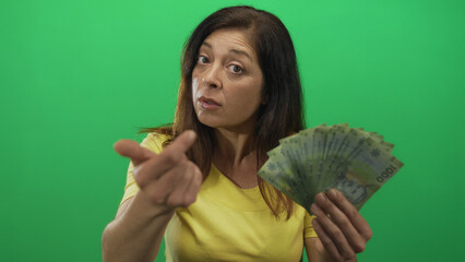 Hispanic woman holds fanned pesos bills and beckons finger in green studio; negotiation persuasion demand.