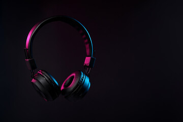 Pair of stylish headphones in air on black background in neon lights, space for text