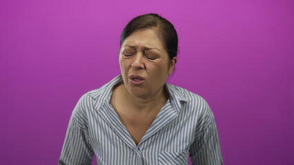 Middle aged hispanic woman sneezing with closed eyes in purple studio setting under bright...