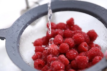 Washing raspberries in sieve at sink, closeup