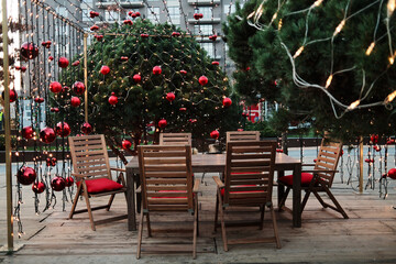 A wooden outdoor seating area is decorated with red ornaments and warm string lights for the holiday season. Concept inviting festive ambience for social gatherings.
