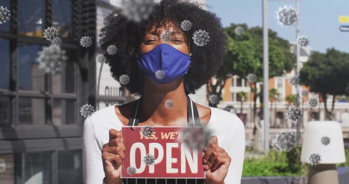 Woman standing outside business raising red OPEN sign, showing open while virus crossing sign or fac
