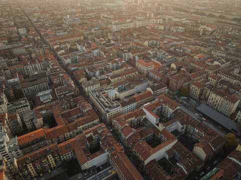 Aerial view of sun-kissed rooftops and symmetrical streets, a warm glow highlighting the urban expanse of Turin, Piedmont, Italy.