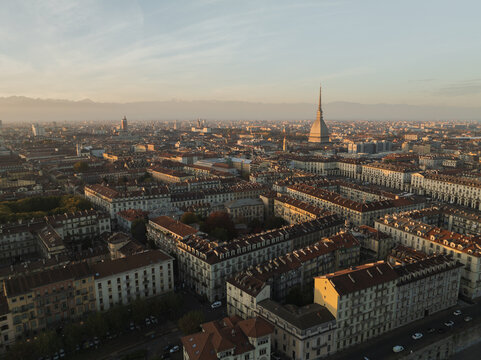 Aerial view of the Mole Antonelliana piercing the skyline, a beacon amidst the muted ochre and terracotta rooftops under the soft, diffused light, Turin, Piedmont, Italy.