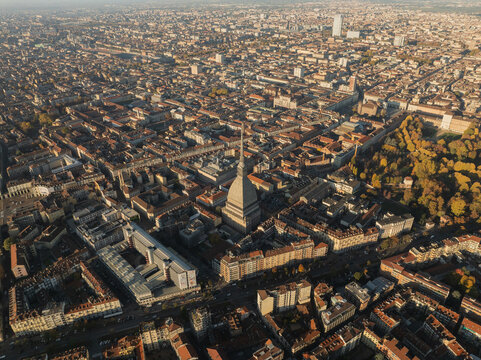 Aerial view of the Mole Antonelliana soaring above the terracotta rooftops and sun-kissed streets, casting long shadows in the autumn light, Turin, Piedmont, Italy.