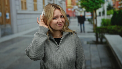 Fototapeta premium Woman wearing sweater gesturing on a city street suggesting communication, conveying emotions in an outdoor urban setting with buildings in the background.