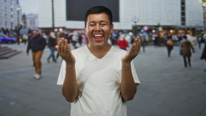 Man wearing white t shirt covering face with hands and smiling with closed eyes on a crowded street...