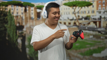Hispanic man wearing white headset and tshirt points finger to red controller on old town street beside historic building and ruins  joy gaming leisure. © Krakenimages.com