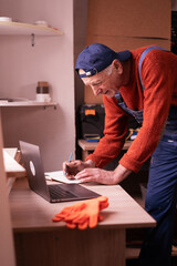 Elderly artisan checking online orders and sales data on computer in woodworking studio. E-commerce business and digital entrepreneurship.