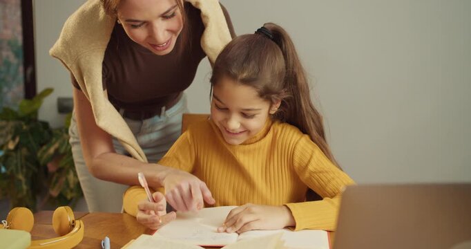 tutor guiding white girl through workbook at kitchen desk