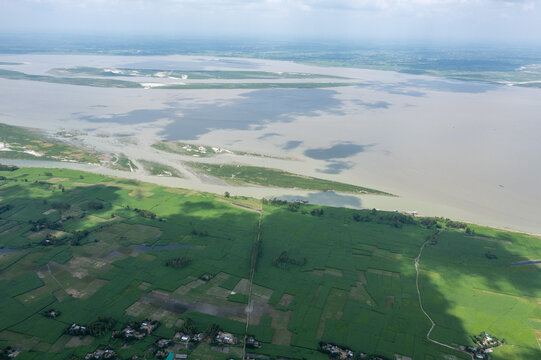 Aerial view of the broad river reflecting the sky, bordered by verdant fields and scattered structures, Sariakandi, Rajshahi Division, Bangladesh.